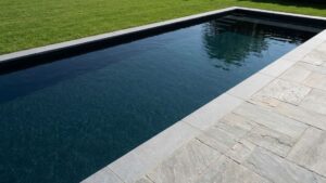 A modern rectangular pool with dark water next to a stone patio.