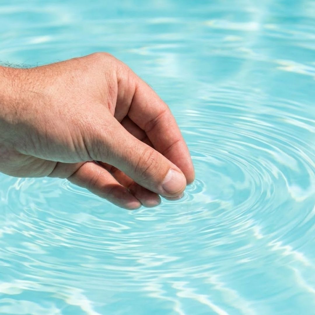 A close-up view shows a hand dipping a small, digital water testing device into the crystalline, clear water of a well-maintained swimming pool.
