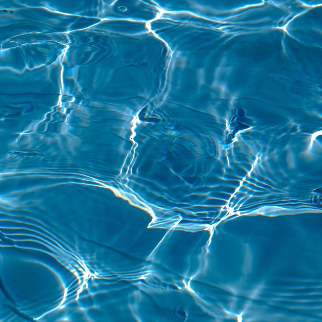 A pristine close-up of crystal clear blue pool water gently rippling in the sunlight, emphasizing cleanliness without heavy chemicals.